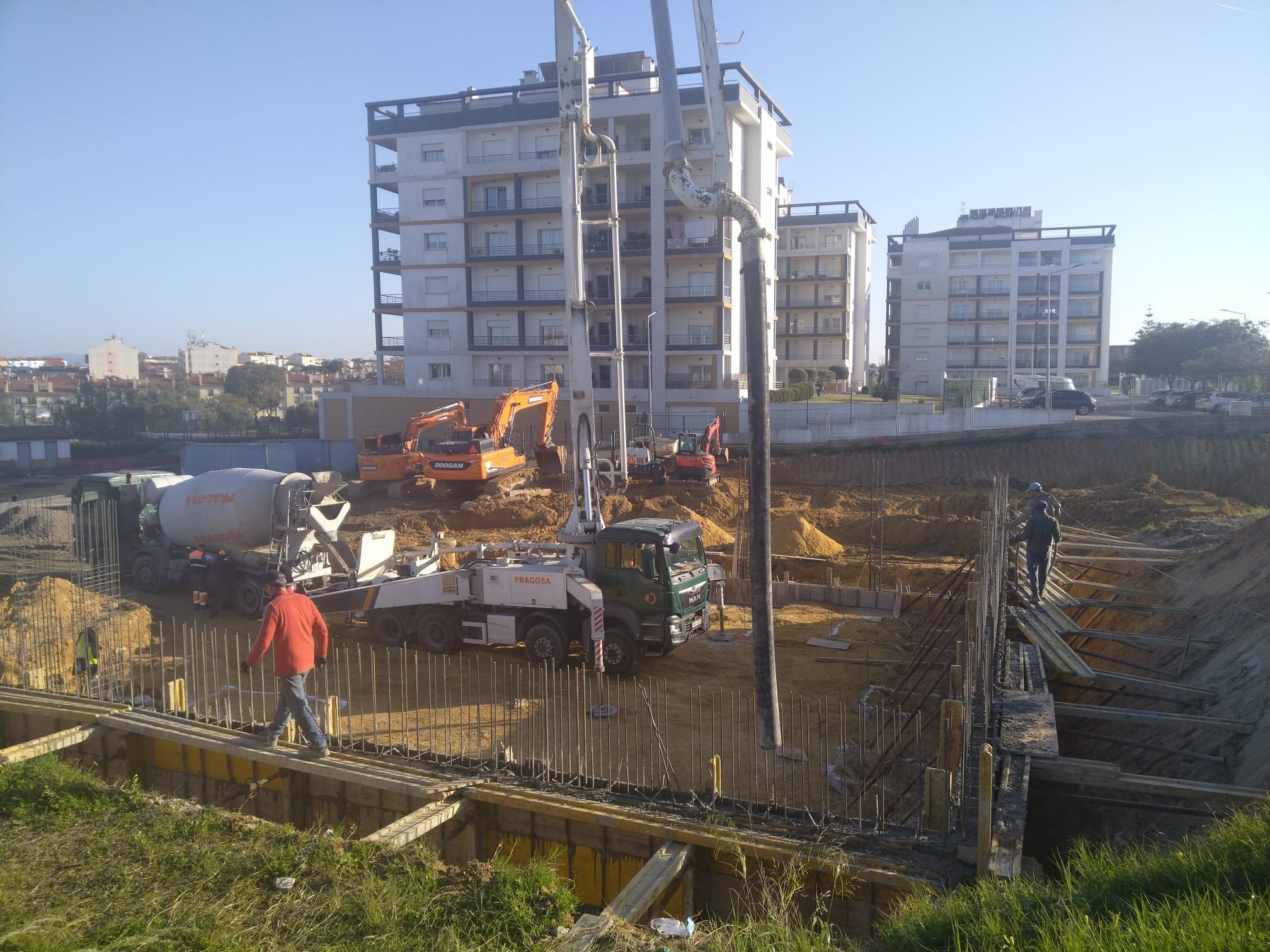 Concrete pour with a mixer truck, pump and excavator, with buildings in the background