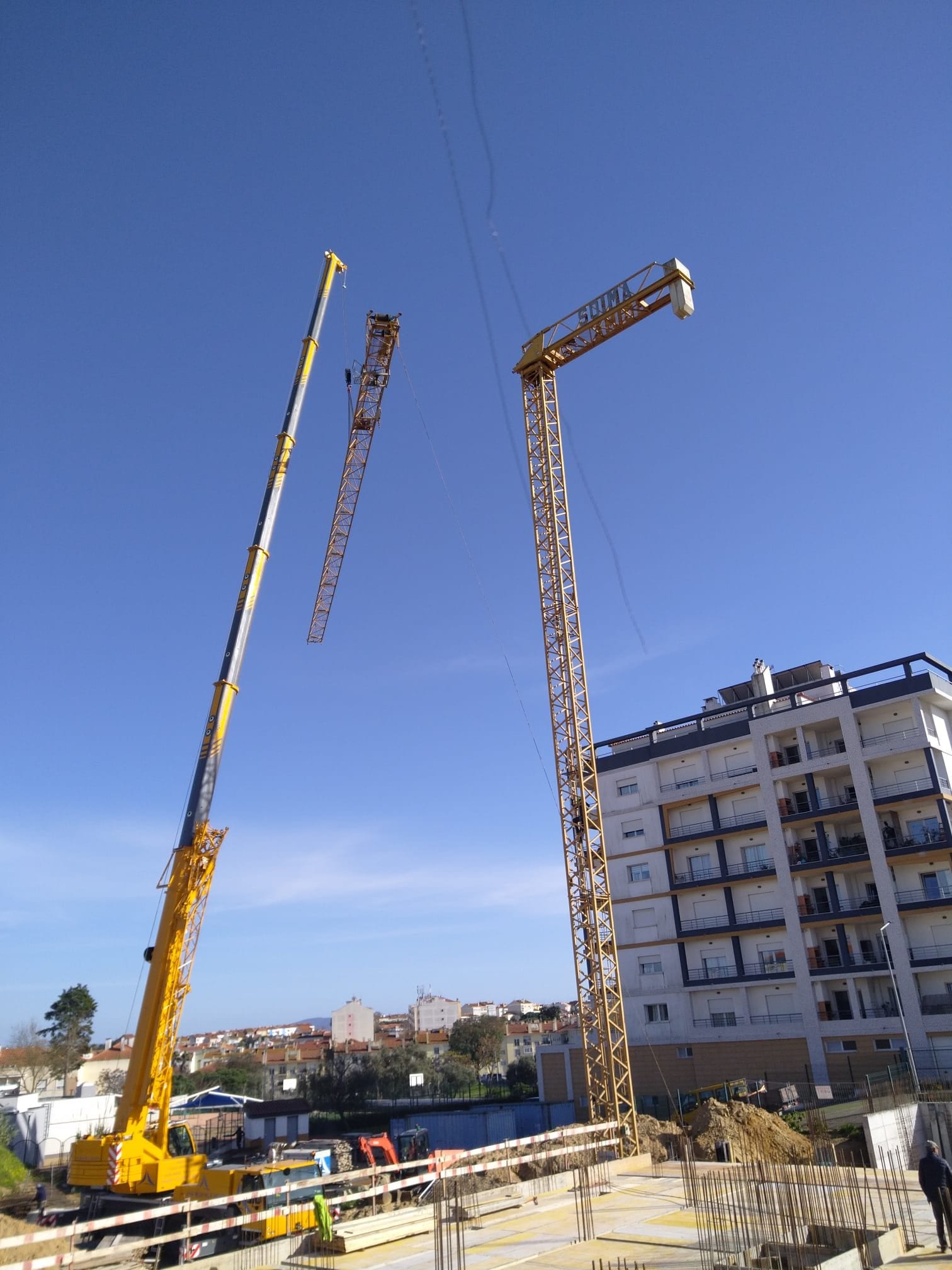 Telescopic crane and tower crane over the site, with a building on the right